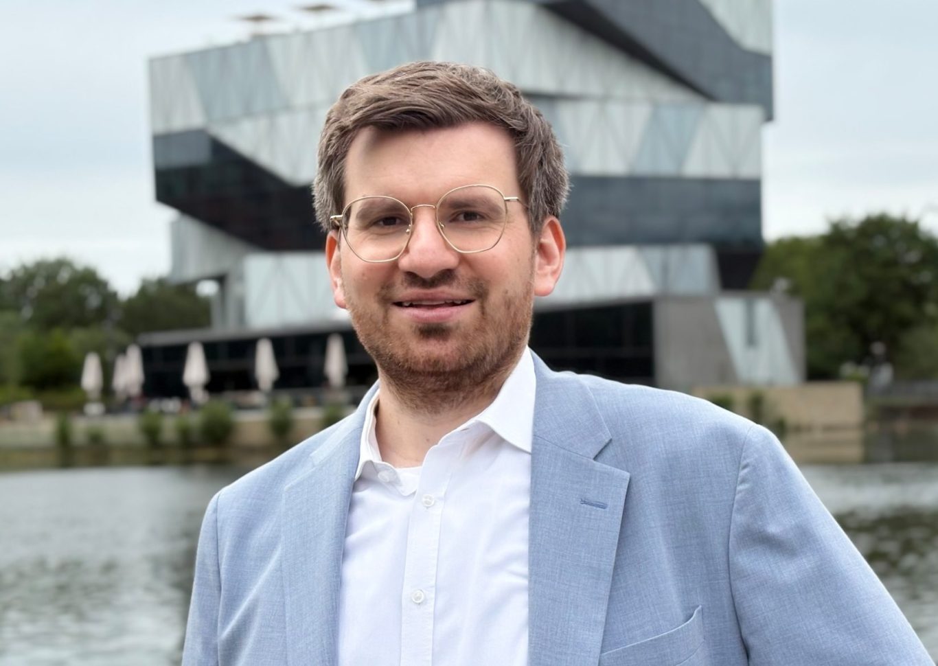 Rechtsanwalt Burkart in hellblauem Jackett steht lächelnd vor Experimenta-Gebäude und Neckar.